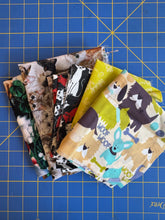 Load image into Gallery viewer, Stack of fabric squares with animal patterns on a blue grid background

